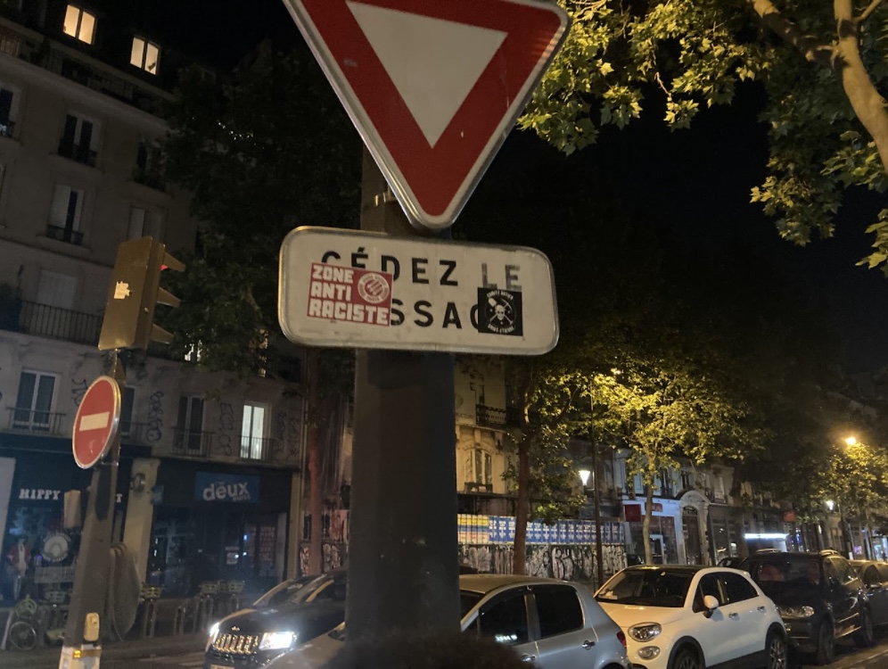 A street sign with stickers on it, one says "Zone Anti Raciste"